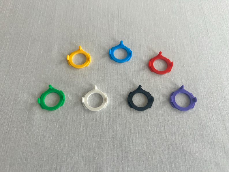 May include: Seven colorful SIM card removal tools in yellow, blue, red, green, white, black, and purple. Each tool has a circular design with a small, pointed tip.