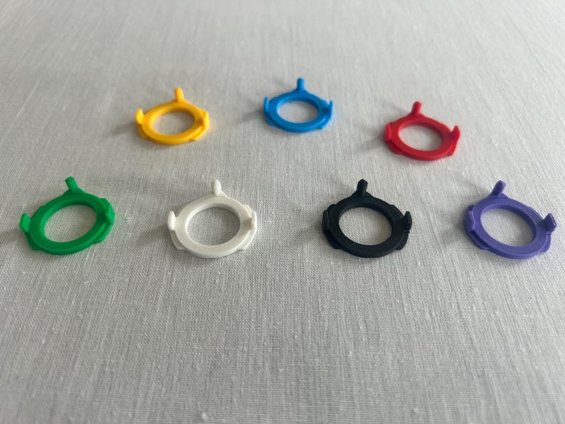 May include: Seven colorful, circular, plastic SIM card removal tools. The tools are in yellow, blue, red, green, white, black, and purple. Each tool has a ring shape with a small, pointed extension.