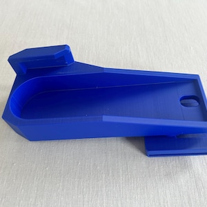 Op de afbeelding: Een helderblauw, 3D-geprint object met een uniek, geometrisch ontwerp. Het heeft een gebogen binnenkant, een rechthoekige basis en een klein gat. Het object is waarschijnlijk een gereedschap of een onderdeel van een groter systeem.