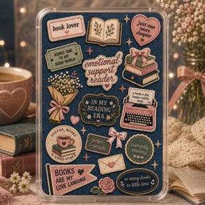 Könnte beinhalten: Ein rechteckiges Display-Board mit dunkelblauem Jeans-Hintergrund, verziert mit verschiedenen gestickten Aufnähern. Die Motive umfassen eine Schreibmaschine, Bücherstapel, einen Blumenstrauß, Herzen und Texte wie book lover, emotional support reader und books are my love language.