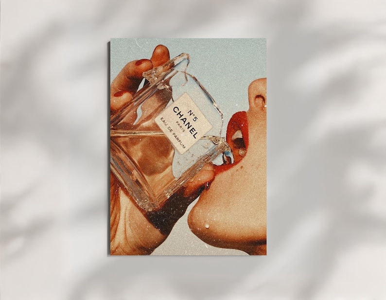 May include: A rectangular wall art print featuring a clear glass Chanel N&deg;5 Eau de Parfum bottle being tilted toward a mouth with bright red lips. The image has a vintage, grainy texture with warm, golden-toned lighting and a light blue background.