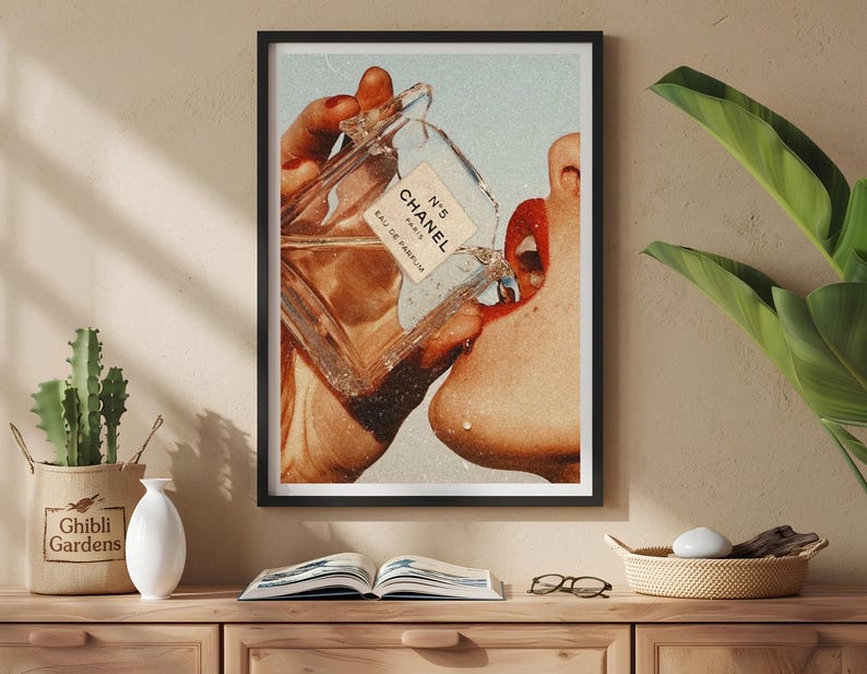 May include: A framed wall art print featuring a vintage-style collage of a hand holding a glass perfume bottle labeled N&deg;5 CHANEL EAU DE PARFUM, with liquid pouring toward a mouth with bright red lipstick, set against a light blue background.