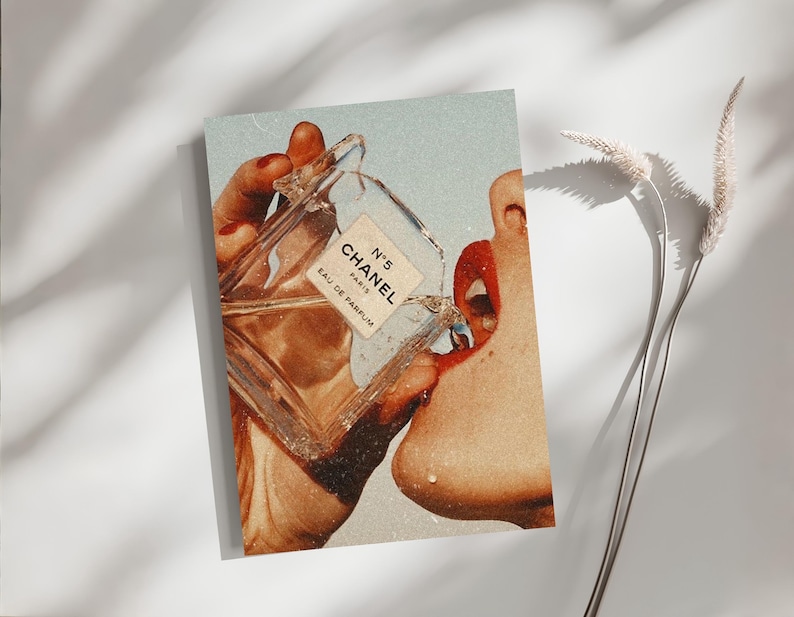 May include: A rectangular art print featuring a vintage-style collage of a clear glass Chanel No. 5 Eau de Parfum bottle being held near a face with bright red lips. The image has a grainy, retro aesthetic with warm, sun-drenched color tones.