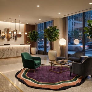 Può includere: Una hall di hotel con reception in marmo, un grande tappeto circolare con anelli concentrici viola, verdi e color pesca, una poltrona verde, una poltrona grigio scuro, un tavolino con piano in vetro e diversi alberi in vaso.