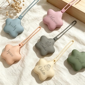 以下が含まれることがあります： 青、ピンク、ピーチ、グレー、クリーム、オリーブグリーンの星型シリコン製おしゃぶりクリップ6点。各クリップには長い柔軟なストラップが付いており、Jocely、Marcie、Jynne、Ember、Odette、Yareliという名前がそれぞれ刻印されています。