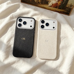 May include: Two smartphone cases with a textured, diagonal weave pattern. One case is black with the gold-colored letters OR, and the other is cream-colored with the letters LF. Both feature a white camera cutout area with three circular lenses.