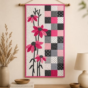 May include: A rectangular fabric wall hanging featuring a vertical split design. The left side displays three appliquéd pink flowers with dark stems on a cream background. The right side consists of a grid of pink, gray, and white squares.