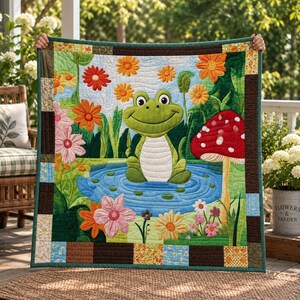 May include: A quilted blanket featuring a central green frog sitting in a blue pond, surrounded by colorful flowers and a large red mushroom with white spots. The quilt has a dark brown and patterned border, with detailed stitching throughout.
