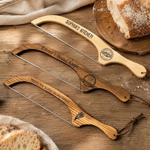 Puede incluir: Tres cuchillos de pan de madera con hojas de acero inoxidable. El cuchillo superior es de color claro y dice "Sophia's Kitchen". El cuchillo del medio es de madera oscura y dice "Emma's Bread Knife". El cuchillo inferior dice "You're the butter to my bread."