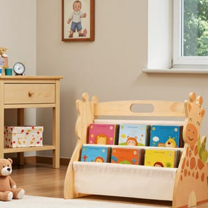 Könnte beinhalten: Ein helles Kinderbücherregal aus Holz mit einem Seitenteil in Giraffenform. Das Möbelstück verfügt über zwei Stoffregale, in denen mehrere bunte Bücher mit Tierillustrationen auf den Einbänden stehen. Das Design ist bodennah.