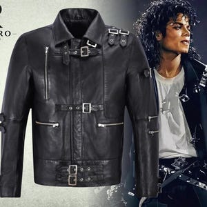 May include: A black leather jacket featuring multiple silver-toned metal buckles across the chest, shoulders, and sleeves, along with several horizontal and vertical zippered pockets. The jacket includes a collar and a Rivaro Jackets logo in the corner.