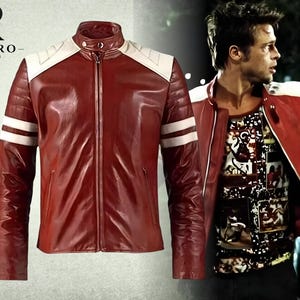 May include: A red jacket with white shoulder panels and two white horizontal stripes on each sleeve. The jacket features a stand-up collar with a snap button closure and a central zipper. The logo RIVARO JACKETS is visible in the top left corner.