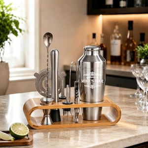 Op de afbeelding: Een roestvrijstalen cocktailshaker-set met een bamboe standaard. De shaker is voorzien van de gegraveerde tekst "Welcome to MIKE'S BAR EST. 2026". De set bevat een jigger, een lange menglepel, een zeef, een stamper en een kurkentrekker.