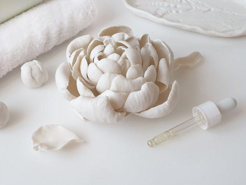 a white flower-shaped object, possibly a ceramic or porcelain piece, along with a dropper and some other white objects on a white surface.