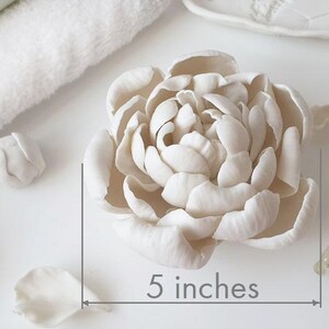 A close-up image of a white flower-shaped object, possibly a ceramic or porcelain piece, with a ruler indicating its size.