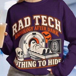 May include: A dark purple long-sleeve sweatshirt featuring a graphic print with the text RAD TECH, RADIOLOGY AFTER DARK, and NOTHING TO HIDE. The design includes a CT scanner, a ghost lying on the scanner bed, a human skull, and a brain scan.