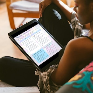 May include: A black tablet displaying a document titled "The Daily Dopamine Menu" is held by a person. The document features a pastel color scheme with text and bullet points. The person is seated, wearing black pants and a striped shirt.