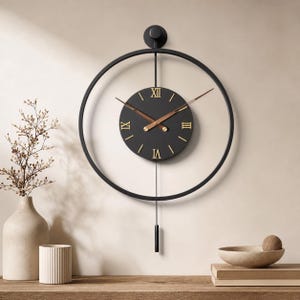 Puede incluir: Un reloj de pared circular negro con una esfera central negra, números romanos dorados y manecillas marrones. El reloj está suspendido dentro de un marco de anillo de metal negro y cuenta con una varilla vertical con un péndulo cilíndrico.