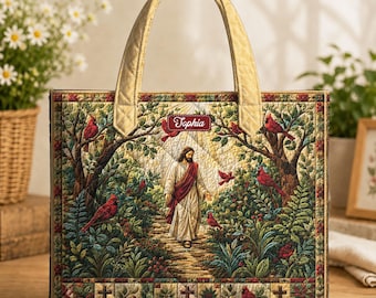 May include: A rectangular quilted tote bag featuring a printed scene of a figure in robes walking along a path through a forest with red cardinal birds. The name Tophia is printed on a red banner. The bag has two gold-colored fabric handles.