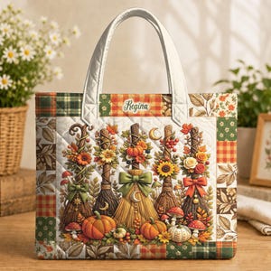Könnte beinhalten: Eine gesteppte Tragetasche mit Patchwork-Bordüre und einem zentralen Motiv aus fünf dekorativen Besen, verziert mit Herbstblumen, Kürbissen und Pilzen. Der Name Regina ist oben aufgedruckt. Die Tasche hat zwei weiße Henkel und einen weißen Steppboden.