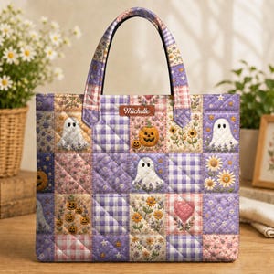 May include: A quilted tote bag featuring a patchwork design of purple and pink gingham squares, floral patterns, ghosts, pumpkins, and a heart. A brown rectangular label with the name Michelle is stitched near the top centre handle.