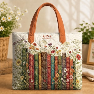 May include: A quilted tote bag with two orange handles, featuring a printed design of colorful vintage book spines interspersed with wildflowers. The name GINA is printed in the center top area. The bag has a diamond-stitched quilted texture.