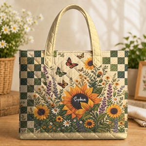 May include: A quilted tote bag featuring a cream-coloured centre panel with a large sunflower, smaller wildflowers, and butterflies. The name Sophia is printed on the sunflower. The sides have a green and cream checkered pattern and gold handles.