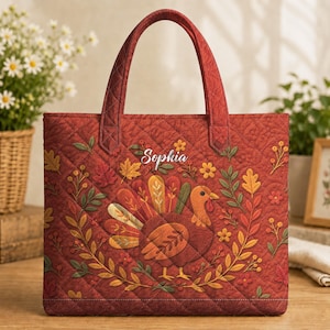 Könnte beinhalten: Eine gesteppte Tragetasche in Dunkelrot mit einer zentralen Grafik eines Truthahns, umgeben von Herbstblättern, Beeren und Blumen. Der Name Sophia ist in weißer Schreibschrift über dem Truthahn aufgedruckt. Die Tasche hat zwei Henkel.