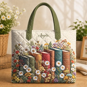Op de afbeelding: Een gewatteerde tas met olijfgroene hengsels en een crèmekleurige stoffen basis. Het ontwerp toont een rij kleurrijke vintage boeken omringd door diverse wilde bloemen en de naam Angela in een sierlijk lettertype aan de bovenzijde.