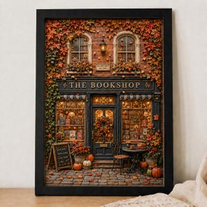 May include: A framed wall art print depicting a brick bookstore storefront titled THE BOOKSHOP. The scene features autumn foliage, two windows with books, a central door with a wreath, a small table with a chair, and pumpkins on a cobblestone path.