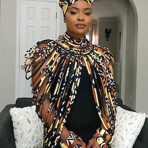May include: A black sleeveless top paired with a matching headwrap, a multi-strand fabric necklace, and two wrist cuffs. The accessories feature a repeating geometric pattern in shades of yellow, orange, white, and black, creating a cohesive set.