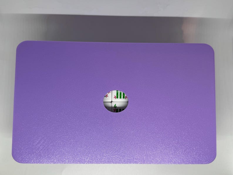 May include: A rectangular, purple object with rounded corners. A small, spherical object with green and white markings is embedded in the centre. The object appears to be a game piece or part of a larger set.