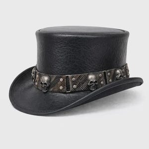 May include: A black top hat with a textured finish, featuring a wide band around the base. The band has a snakeskin-like pattern and is decorated with multiple silver-toned metal skull ornaments and small circular studs spaced evenly throughout.