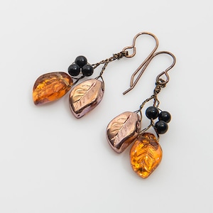 May include: A pair of dangle earrings featuring copper wire, black beads, and orange glass leaves.