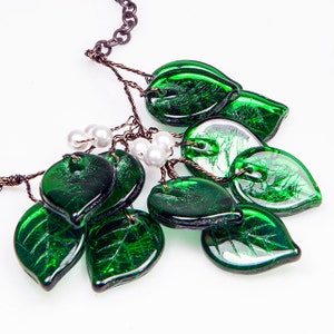 May include: A green glass leaf necklace with a brown chain and white pearl accents. The leaves are made of textured glass and have a metallic sheen.