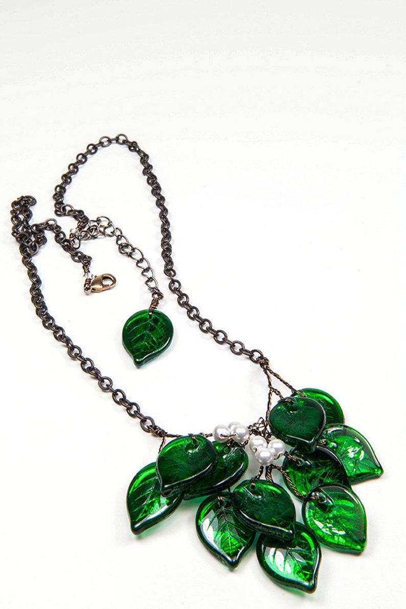 May include: A green glass leaf necklace with a silver chain and a small green glass leaf pendant. The necklace features a cluster of green glass leaves with white pearl accents.