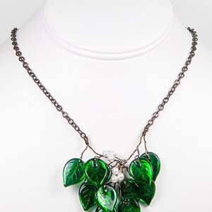 May include: A delicate necklace featuring a cluster of green glass leaves and white pearl accents. The leaves are arranged in a cascading pattern, creating a whimsical and elegant look.