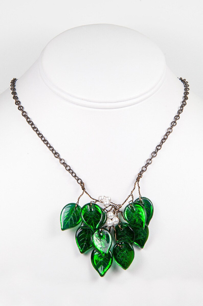 May include: A delicate necklace featuring a cluster of green glass leaves and white pearl accents. The leaves are arranged in a cascading pattern, creating a whimsical and elegant look.