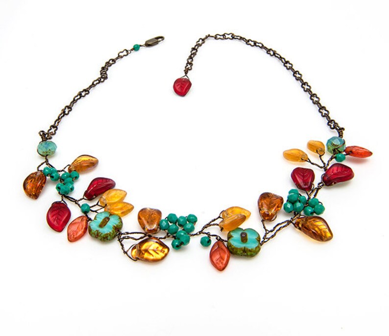May include: A delicate necklace with a leafy design featuring orange, red, and turquoise glass beads. The necklace is made with wire and has a simple chain closure.