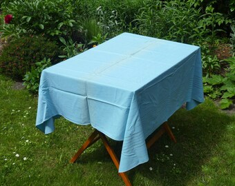 May include: A light blue tablecloth draped over a wooden table, set up outdoors on a grassy lawn.
