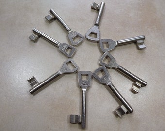 May include: A collection of eight silver keys arranged in a star shape on a light gray surface.