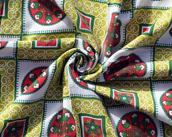 May include: A white fabric with a repeating pattern of green, red, and white circles and squares. The fabric is folded in a spiral shape.
