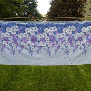 Può includere: Un tessuto floreale blu e bianco con un motivo ripetitivo di fiori e viti. Il tessuto è appeso a uno stendino.