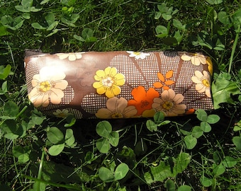 May include: A brown zippered pencil case with a retro floral pattern featuring yellow, orange, and white flowers on a brown background.