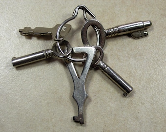May include: A set of four antique keys with a silver finish. The keys are attached to a metal ring. The keys have different shapes and sizes.