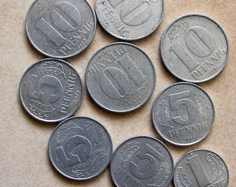 May include: A collection of nine silver German coins with different denominations, including 1, 5, and 10 Pfennig. The coins feature various designs, including a stylized eagle, a wreath, and a wheat stalk. The coins are dated from 1955 to 1979.