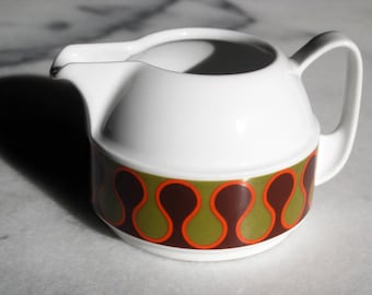 May include: White ceramic creamer with a brown, green, and orange geometric pattern. The creamer has a rounded body and a spout on one side.