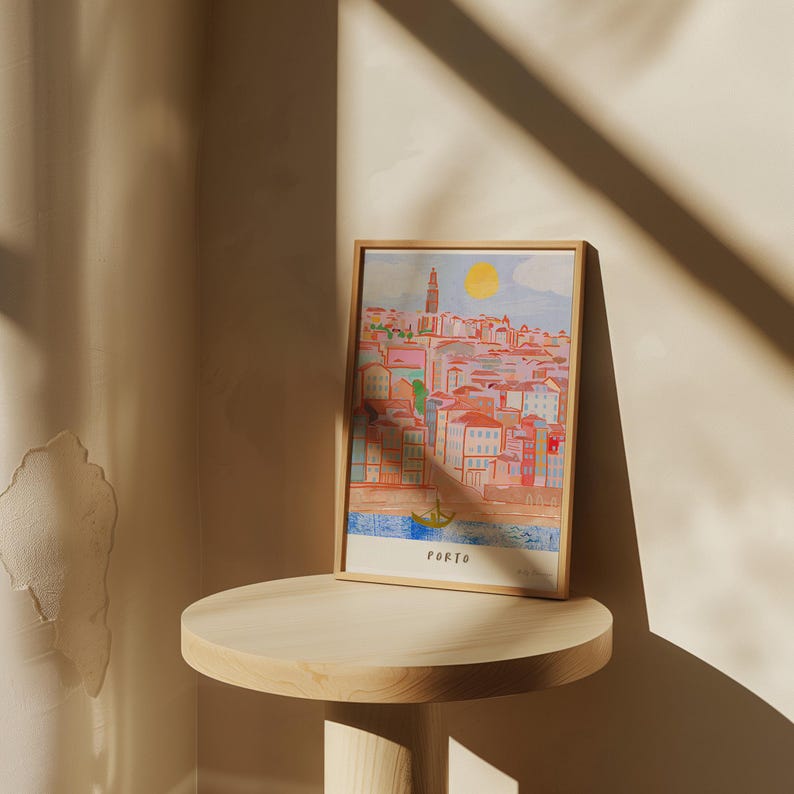 May include: A framed illustration of the city of Porto, Portugal. The illustration is in a colorful, cartoon style and depicts a cityscape with buildings, a river, and a boat. The frame is wooden and has a light brown finish. The text "PORTO" is printed at the bottom of the illustration.