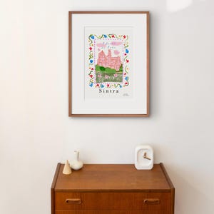 May include: A framed illustration of a pink castle with a blue sky and white clouds. The castle is surrounded by a colorful floral border. The text "Sintra" is written below the castle.
