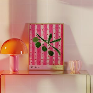 Puede incluir: Una impresi&oacute;n enmarcada de una pintura de una rama de olivo con aceitunas verdes sobre un fondo a rayas rosa y blanco. La impresi&oacute;n se titula "Olive."